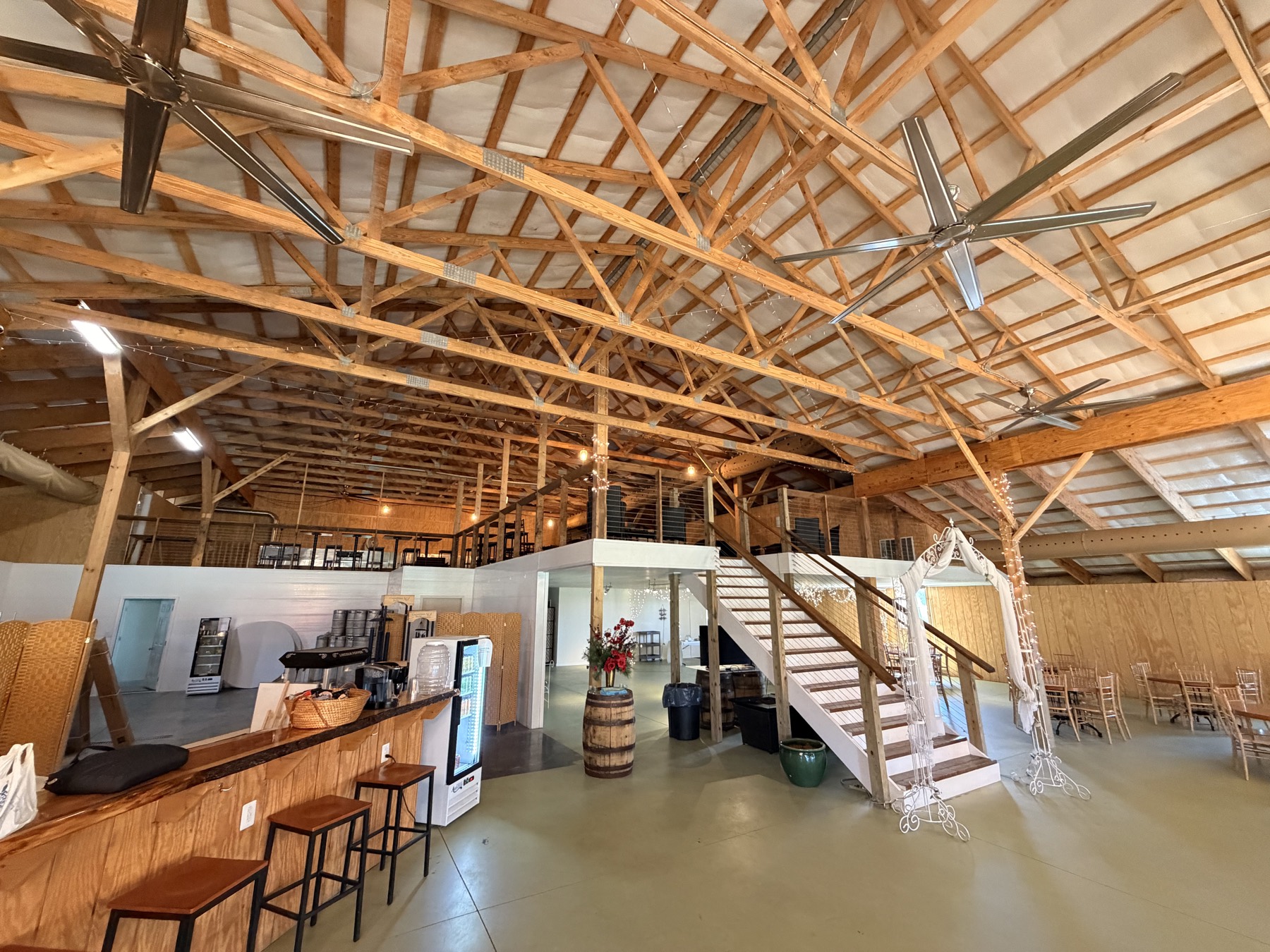 The main event space at floor level — grand stairway to the mezzanine, wedding arch, and exposed timber trusses